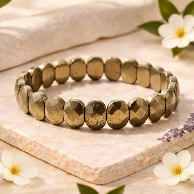 Gold beaded bracelet on a light stone surface with flowers