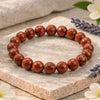 Red beaded bracelet on a stone surface with flowers