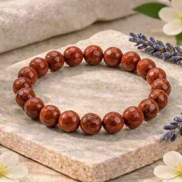 Red beaded bracelet on a stone surface with flowers