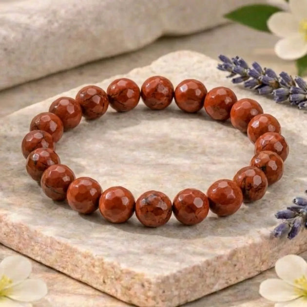 Red beaded bracelet on a stone surface with flowers