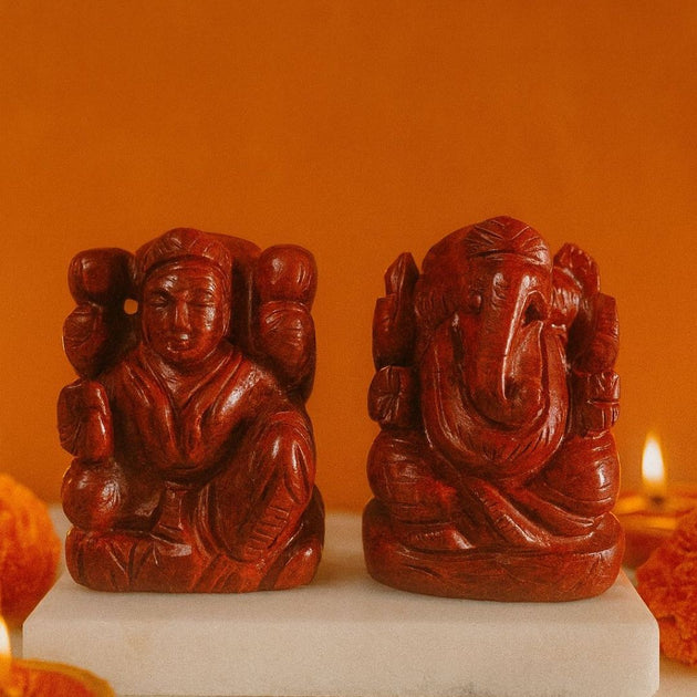 two crystal stone carvings of lakshmi ganesha on a white platform with an orange background