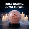 Rose quartz crystal ball with a spiral design on a dark background with candles.