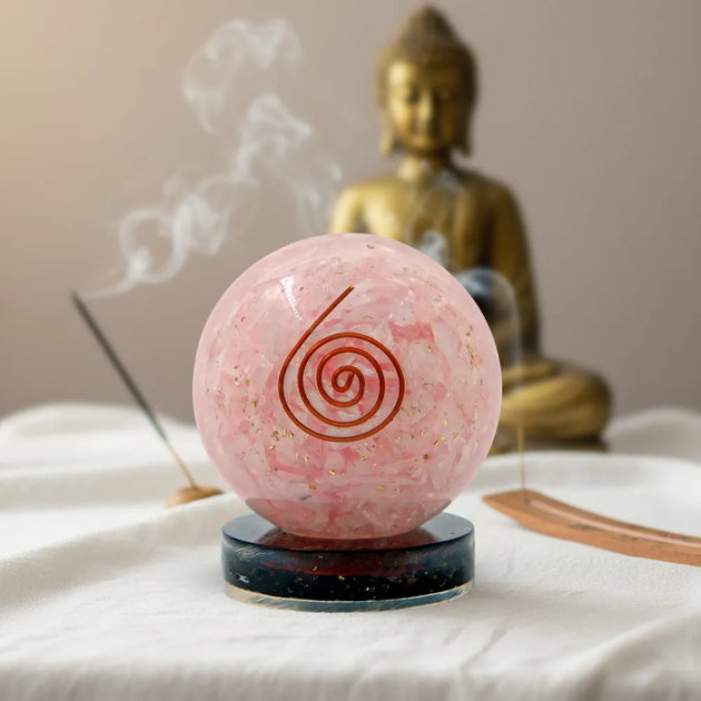 Pink crystal ball with a spiral design on a stand, placed in front of a Buddha statue.