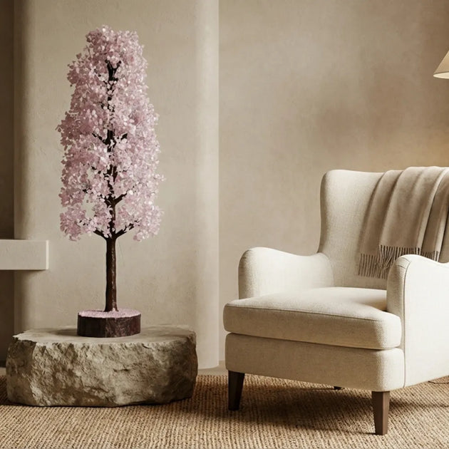 Decorative pink tree on a stone base next to a beige armchair in a room with neutral walls.
