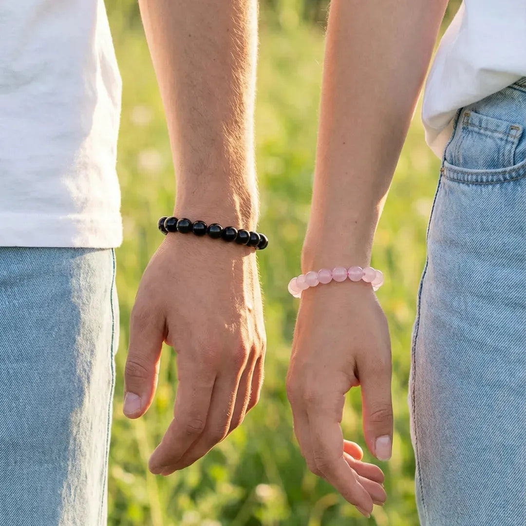Two people holding hands with bracelets on, standing in a grassy field.