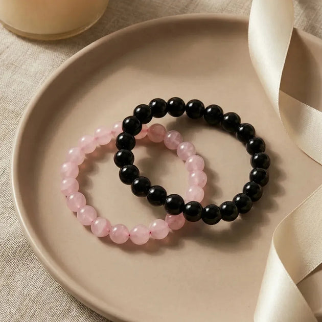 Two beaded bracelets, one pink and one black, on a beige plate with a neutral background.