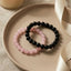 Two beaded bracelets, one pink and one black, on a beige plate with a neutral background.