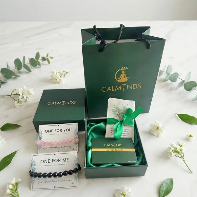 Gift set with 'Calminds' branding including a bracelet, card, and book on a white background with greenery.