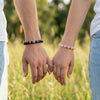 Two people holding hands with bracelets on, standing in a grassy field.