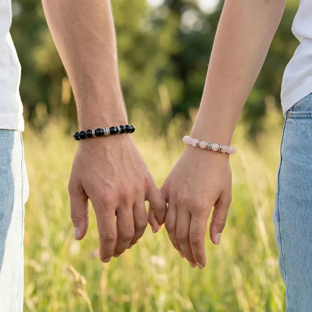 Two people holding hands with bracelets on, standing in a grassy field.