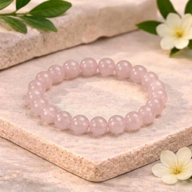 Pink beaded bracelet on a light wooden surface with flowers and leaves.