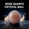 Rose quartz crystal ball with a spiral design on a dark background with candles
