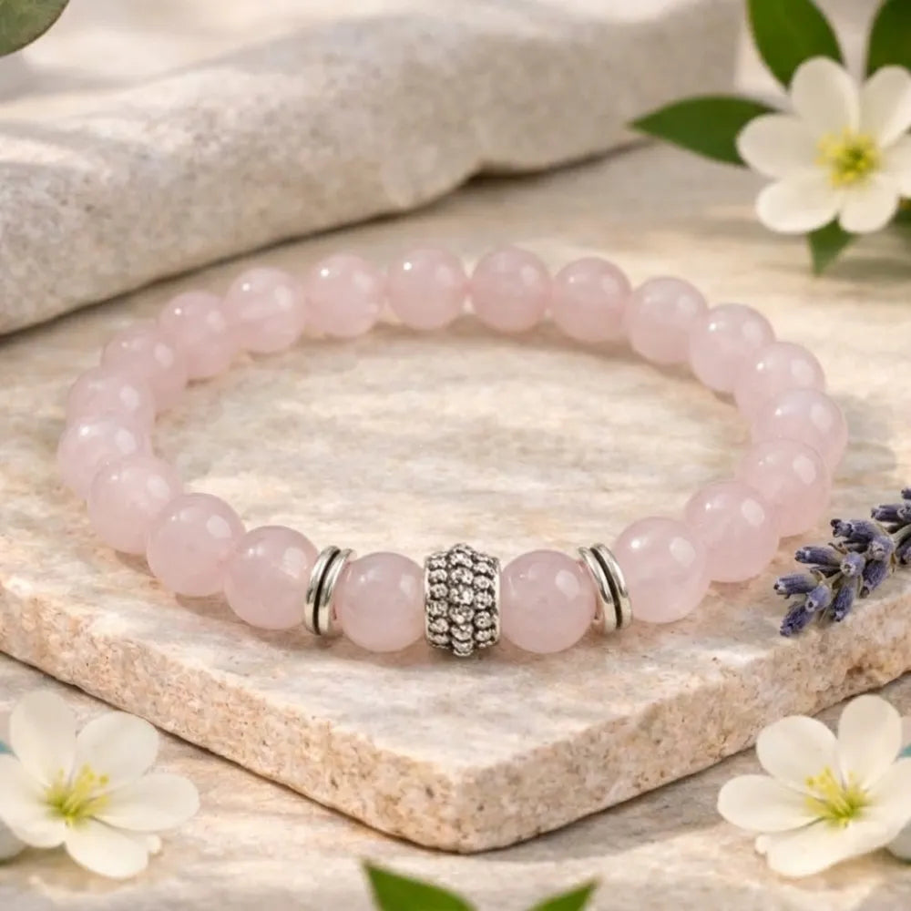 Pink beaded bracelet with silver charms on a stone surface with flowers