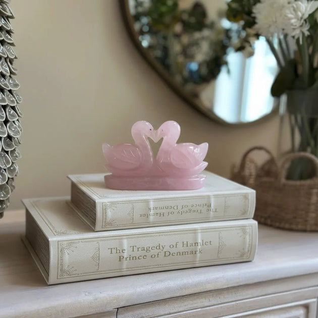 Pink swan figurine on top of a book titled 'The Tragedy of Hamlet Prince of Denmark' on a decorative surface.