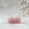 Rose quartz sculpture of two swans on a marble surface with a blurred floral background