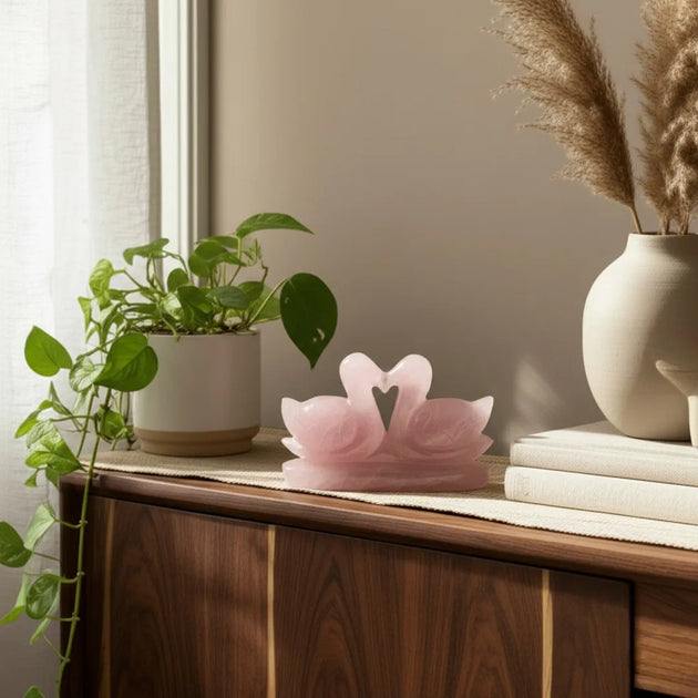 Pink swan-shaped lamp on a wooden dresser with a plant and books in the background