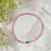 Pink beaded bracelet with a blue evil eye charm on a white fabric background with flowers.