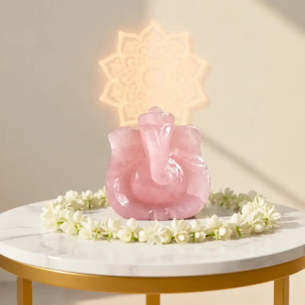 Rose Quartz Ganesha idol lit from behind on a white table with flowers