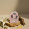 Pink crystal with silver accents on a wooden stand, surrounded by flowers and leaves on a beige background