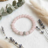Pink beaded bracelet with silver accents on a white surface with eucalyptus and lavender.