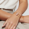 Close-up of a hand wearing a gold bracelet with pink gemstones on a neutral background