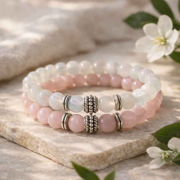 Stack of pink and white beaded bracelets on a stone surface with flowers.
