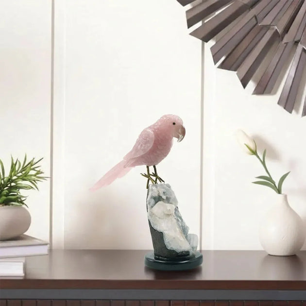 Decorative pink parrot sculpture on a stand with plants and a lamp in the background