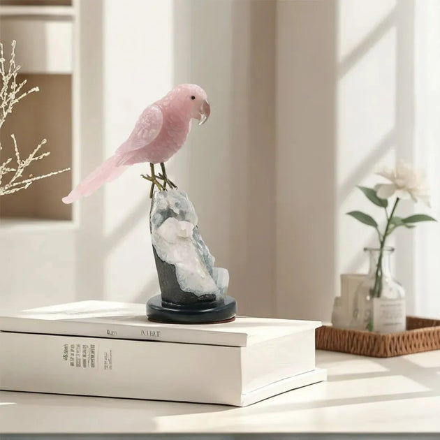 Pink parrot figurine on a decorative stand on top of a book with a blurred indoor background