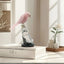 Pink parrot figurine on a decorative stand on top of a book with a blurred indoor background