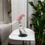 Pink parrot figurine on a white table with plants and a sofa in the background