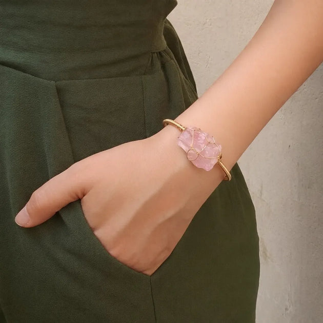 Person wearing a gold bracelet with a pink stone on a plain background