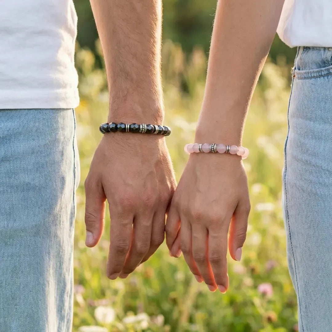 Two people holding hands with bracelets on, standing in a grassy field.