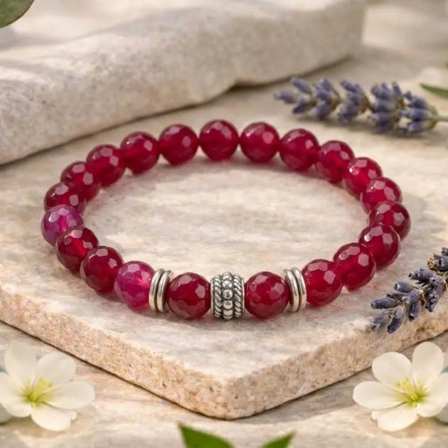Red beaded bracelet with silver charm on a stone surface with flowers and lavender.