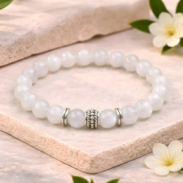 White beaded bracelet with a silver charm on a wooden surface with flowers