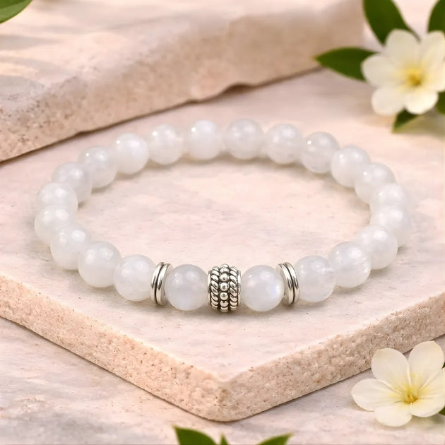White beaded bracelet with a silver charm on a wooden surface with flowers