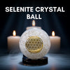 Selenite crystal ball with a gold symbol on a dark background with candles
