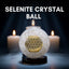 Selenite crystal ball with a gold symbol on a dark background with candles