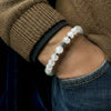 Close-up of a person wearing a white beaded bracelet with a brown sweater and blue jeans.
