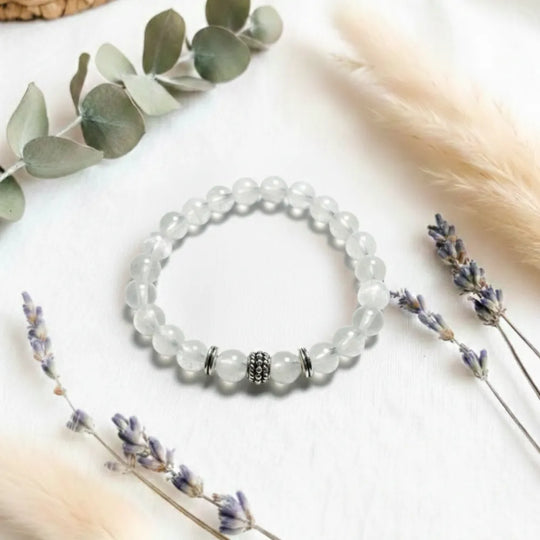 White beaded bracelet on a white surface with lavender flowers and eucalyptus leaves.