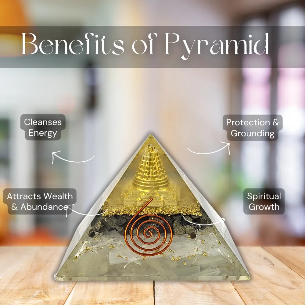 A triangular crystal pyramid with a gold-toned top, black middle band, and copper spiral detail, displayed on a wooden surface with blurred background and overlaid text reading 'Benefits of Pyramid' and callouts about energy cleansing, protection, wealth, and spiritual growth.