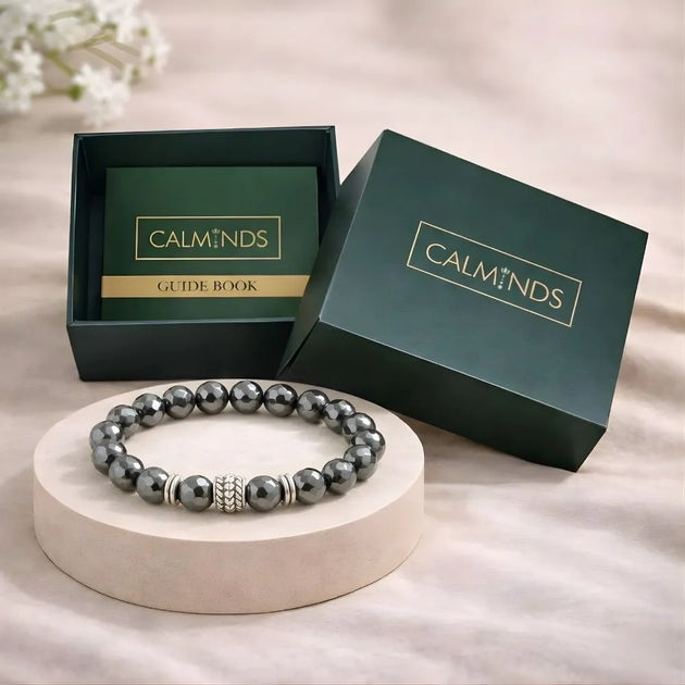 Gray beaded bracelet on a white stand with 'CALMINDS' branded box in the background