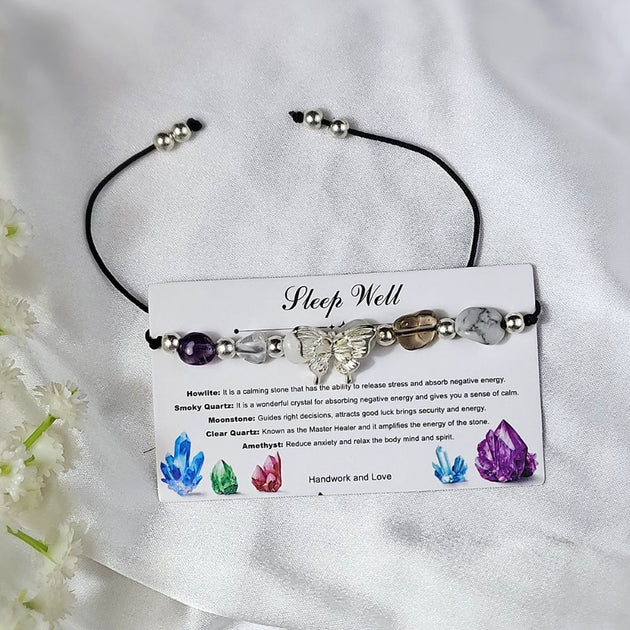 Crystal bracelet with stones on a card explaining their properties, on a white fabric background with flowers.