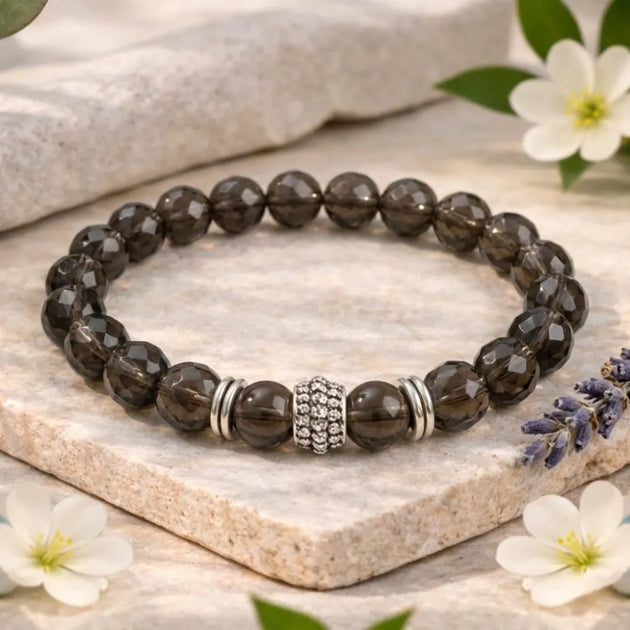 Smoky stone beaded bracelet with a silver clasp on a stone surface with flowers.