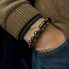 Close-up of a hand wearing a beaded bracelet with a brown sleeve and blue jeans.