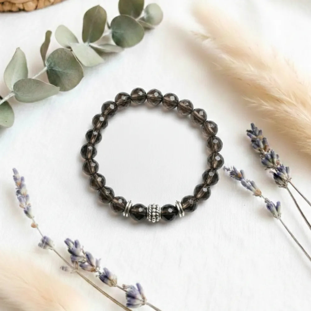 Black beaded bracelet on a white surface with lavender and eucalyptus leaves