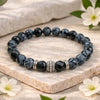 Black and gray beaded bracelet with silver accents on a stone surface with flowers.