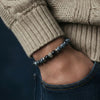 Close-up of a person wearing a bracelet with a dark blue and silver design, against a neutral background.