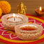 Decorative candles in small bowls on a colorful mat with a statue and marigold flowers in the background.
