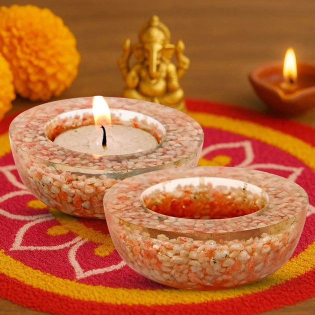 Decorative candles in small bowls on a colorful mat with a statue and marigold flowers in the background.
