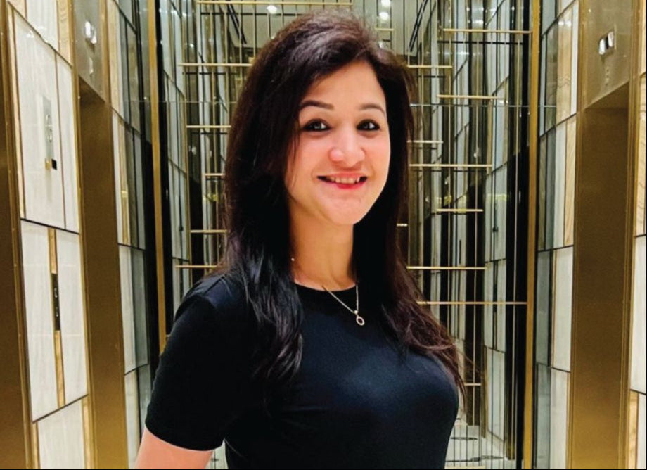 Sweeny Panjrath, the founder of Calminds, in the image, a Woman in a black outfit standing in a modern indoor setting with gold and glass walls